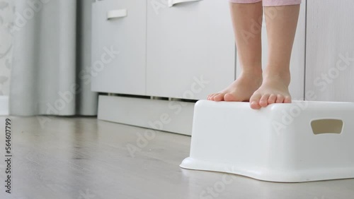 Small children's legs getting up on the step. Small children's legs stand on a special children's stand on kitchen. toddler girl's feet standing on step stool in kitchen. Small child helps at home photo