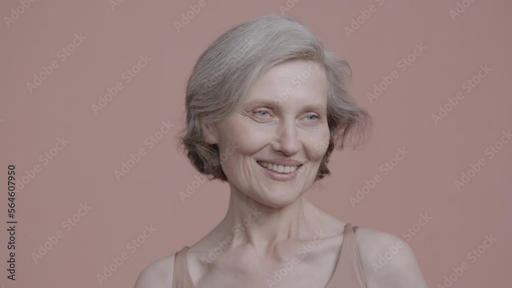 Portrait of beautiful 60s grey-haired mature senior adult female posing without makeup against light brown background. Studio shot, soft lighting. No make up, clean skin. Shot with ARRI Alexa Mini LF Portrait of beautiful 60s grey-haired mature senior adult female posing without makeup against light brown background. Studio shot, soft lighting. No make up, clean skin. Shot with ARRI Alexa Mini LF