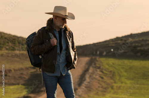 Adult man in cowboy hat on dirt road against sky © WeeKwong
