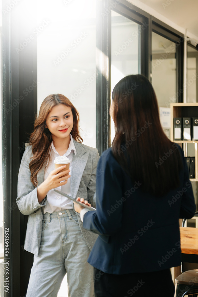 Happy two Asian business woman holding coffee cup in coworking office.