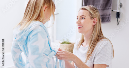 Girl, mother and bathrobe in a bathroom for cleaning, wellness and hygiene in their home together. Children, washing and woman help child with gown after shower, bond and relax while talking