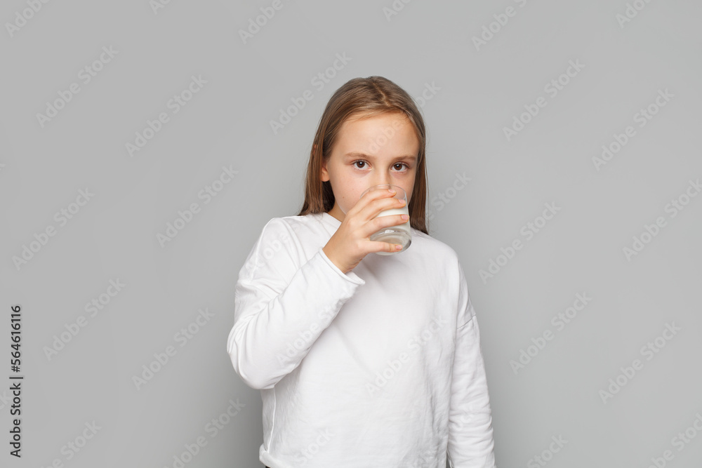 Adorable child girl enjoying drinking milk on a grey background Adorable child girl enjoying drinking milk on a grey background