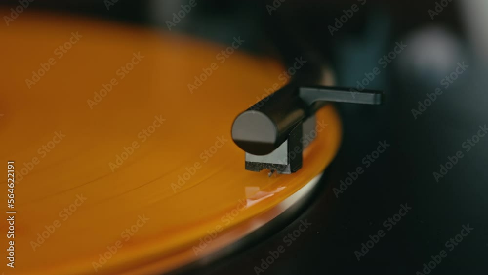 Close up on turntable stylus touching slowly turning orange vinyl record. Vintage and classy record player collection. DJ or music production equipment