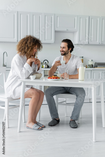full length of happy young man having breakfast with curly girlfriend in kitchen.