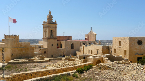 Gozo Cathedral, or Il-Katidral ta' G_awdex.  Sunshine and blue sky with Maltese flag