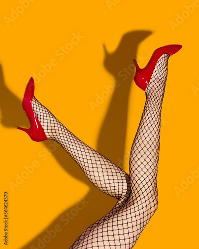 Contemporary art collage. Female slim legs in fishnet socks and red heeled shoes on bright yellow background. Pop art photography. Vivid colors. Concept of creativity, imagination, artwork, lgbt, fun.