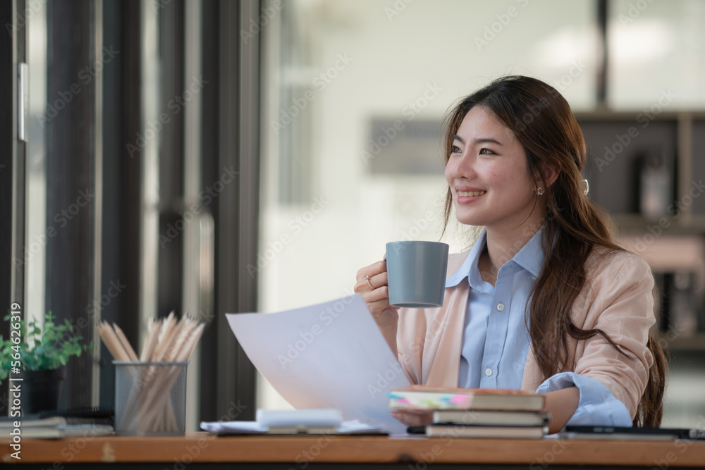 An attractive businesswoman holding a cup of hot drink and looking away with a smile while sitting in an office. An attractive businesswoman holding a cup of hot drink and looking away with a smile while sitting in an office.