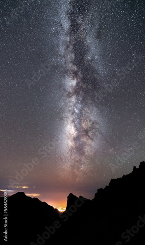 Milky way over the lights of the city and mountain silhouette