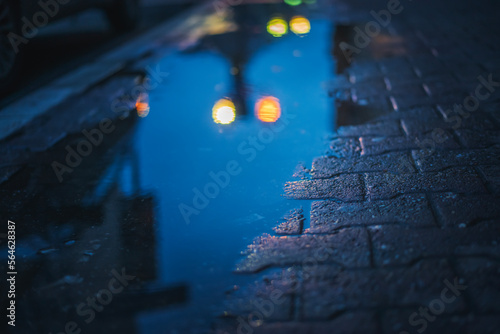 A puddle on the sidewalk in the city with the reflection of night city lights. Abstract urban background