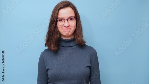 A smug smile. Portrait of a female student in glasses and a sweater with a smug smile on a blue background, 4K. emotion facial expression. feelings and people reaction. photo