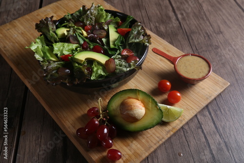 Healthy vegetable salad served on a wooden tray with avocado  grapes  lemon  cherry tomatoes  and dressing
