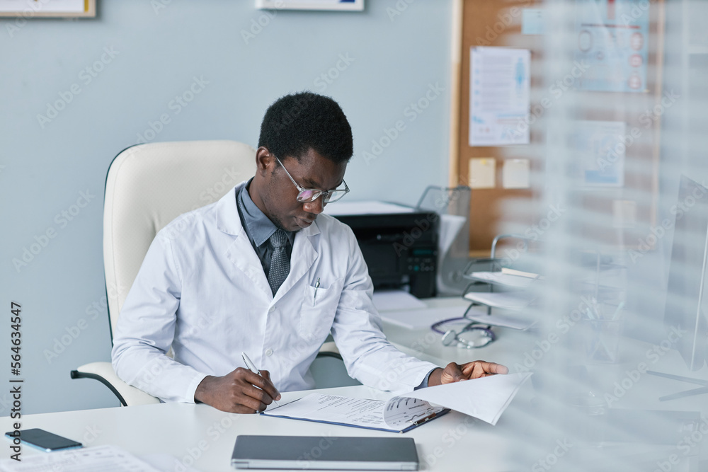 Young black doctor filling papers at desk in office working in clinic Young black doctor filling papers at desk in office working in clinic
