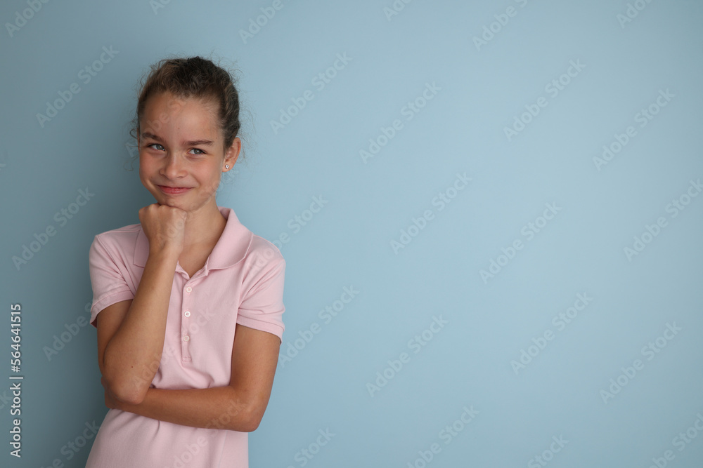 Little emotional teenage girl in pink shirt 11, 12 years old on an isolated blue background. Children's studio portrait. Place text to copy space for caption, advertising children's goods.