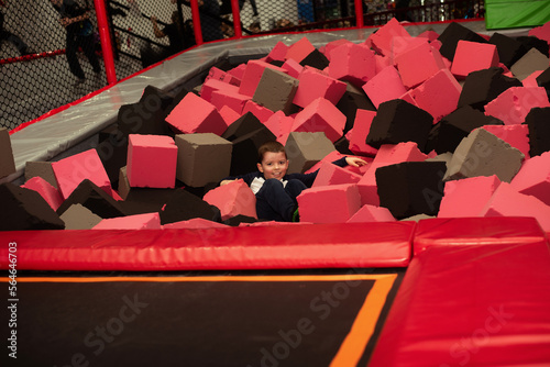 Little six-year-old boy smiles while lying in foam cubes in a trampoline entertainment center