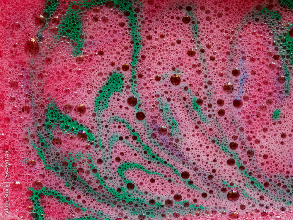 Pink foam with green veined, marbled pattern of dissolve aromatic bath bomb in water.