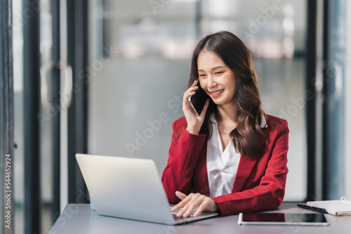 Happy young asian woman talking on the mobile phone while sitting at her working place in office.