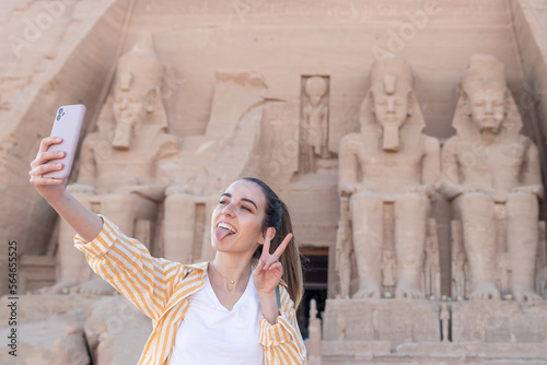 Young woman tourist taking a selfie with tounge out and peace out sign in Abu Simbel temple, Egypt