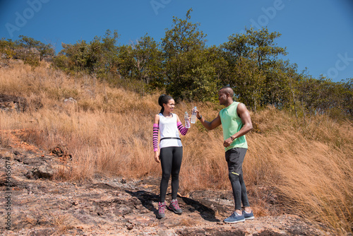 Athletic man and woman jogging outdoor in summer forest stop drinking water. African American couple running sport training together. Colleague workouts running and healthy lifestyle.