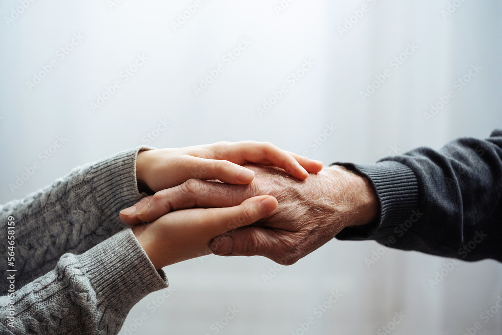 Closeup of hands of old man and a young female hands. Senior man, with caregiver indoors. Helping hand for the elderly concept with young hand holding old hand. - obrazy, fototapety, plakaty 