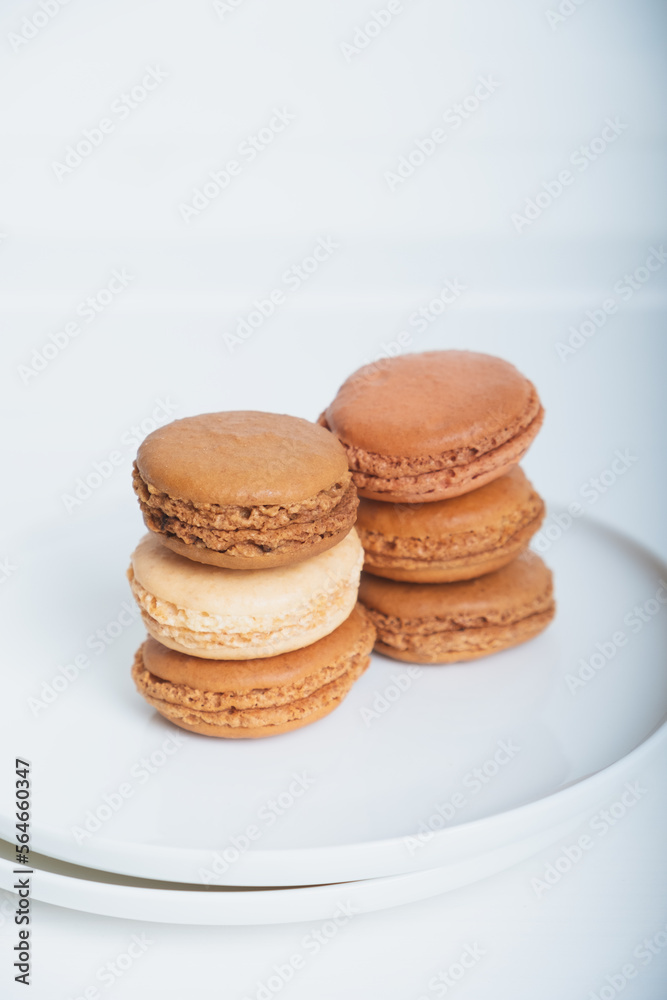 Stack of delicious freshly baked caramel, coffee and vanilla flavoured macaron confections on white plate against white background. French sweet food speciality.