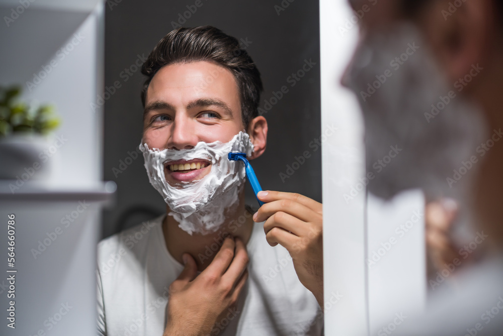Man shaving beard while looking himself in the mirror.	
