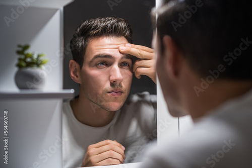 Man looking at his wrinkles while standing in front of mirror. 