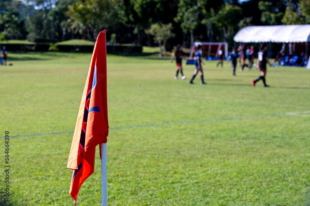 Orange corner flag from a football pitch, seeing group of players, coaches, staffs and parents getting together as a team in a background. Atmosphere from a youth football tournament in a summer time. Orange corner flag from a football pitch, seeing group of players, coaches, staffs and parents getting together as a team in a background. Atmosphere from a youth football tournament in a summer time.
