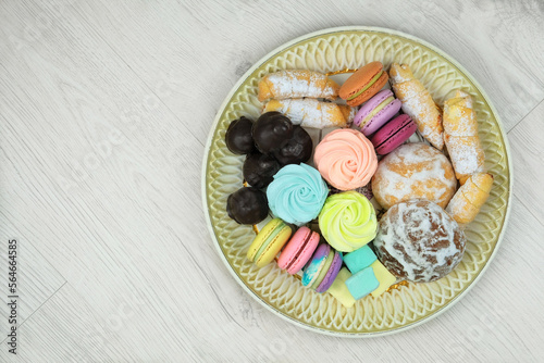 Sweet desserts in plate for the holiday on wood background. Marshmallows, macaroons, cake and chocolate candies in a large plate. Top view.