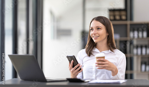 Smiling beautiful Asian businesswoman analyzing chart and graph showing changes on the market and holding smartphone at office.
