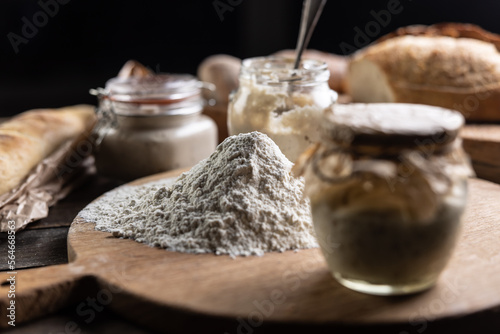 A scoop of smooth flour and around it jars with yeast and fresh bread