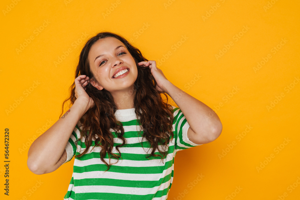 Smiling girl touching her hair over yellow wall