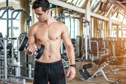 Young man lifting dumbbell and working out on his biceps at gym.