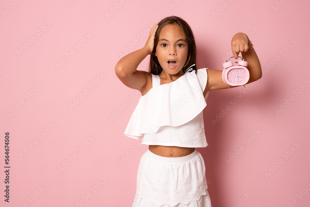 Image of cheerful amazed little girl child standing isolated over pink background. Looking camera pointing to clock alarm. Image of cheerful amazed little girl child standing isolated over pink background. Looking camera pointing to clock alarm.