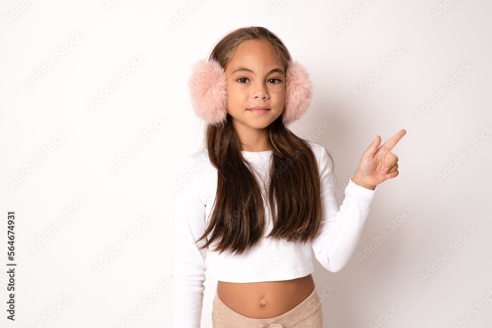 Little girl in winter clothing pointing finger up standing over white background. Little girl in winter clothing pointing finger up standing over white background.