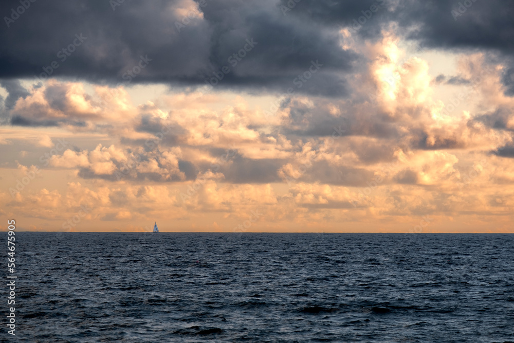 sunset in the sea with a lonely sail bot in the horizon
