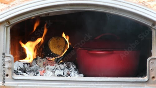 Cooking in stone oven.  Cast iron pot in wood-fired oven burning flames. 