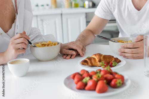 cropped view of young couple holding hands near delicious breakfast on table.