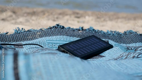 Solar panel charging a mobile phone on a beach. Portable powerbank solar charger in sunlight. Sun energy.