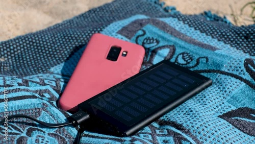 Solar panel charging a mobile phone on a beach. Portable powerbank solar charger in sunlight. Sun energy.