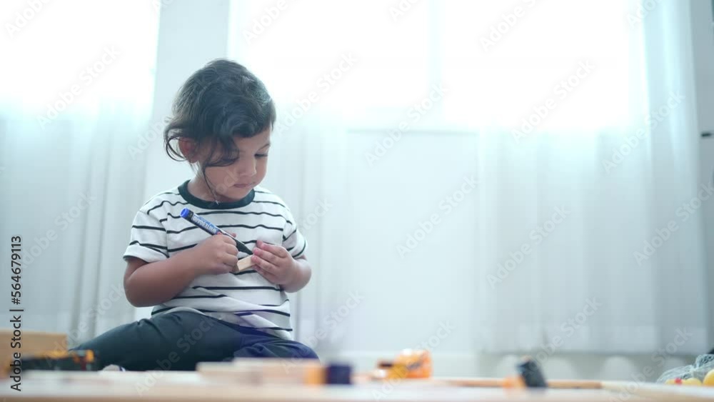 The little boy concentrated on drawing lines with a magic pen on a piece of wood in his hand. The little boy concentrated on drawing lines with a magic pen on a piece of wood in his hand.