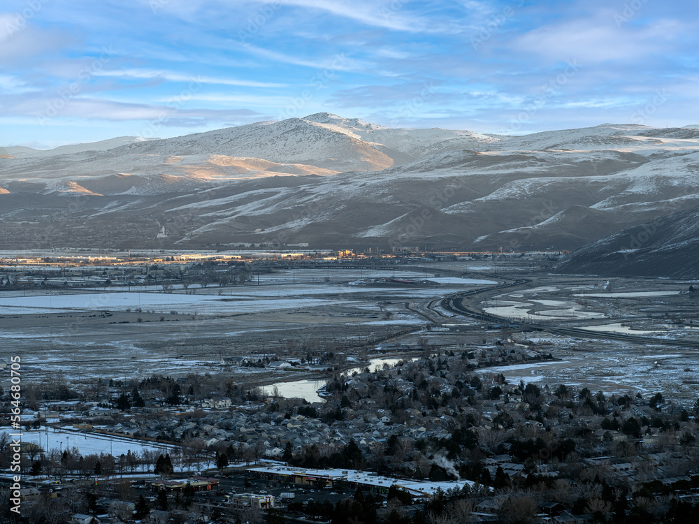 Aerial view of East Sparks Nevada along Veterans Parkway during winter with Snowcapped Mountains, frozen rivers and lakes and early morning traffic.
