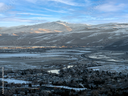Aerial view of East Sparks Nevada along Veterans Parkway during winter with Snowcapped Mountains, frozen rivers and lakes and early morning traffic.