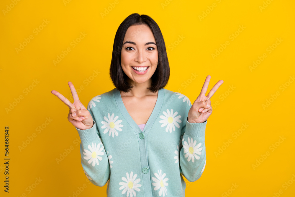 Photo of funny cheerful white teeth smiling korean girl wear teal cardigan daisy print show v-sign peace everyone isolated on yellow color background Photo of funny cheerful white teeth smiling korean girl wear teal cardigan daisy print show v-sign peace everyone isolated on yellow color background