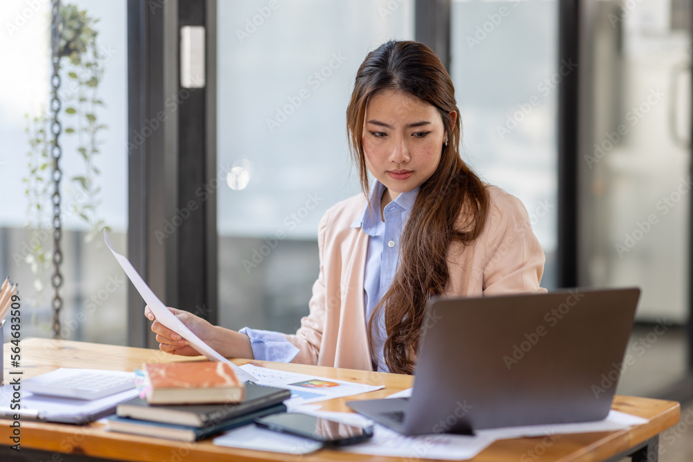 Thai Asian businesswoman working inside office with documents and laptop, worker paperwork calculates financial indicators smiling and happy with success and results of achievement and work Thai Asian businesswoman working inside office with documents and laptop, worker paperwork calculates financial indicators smiling and happy with success and results of achievement and work