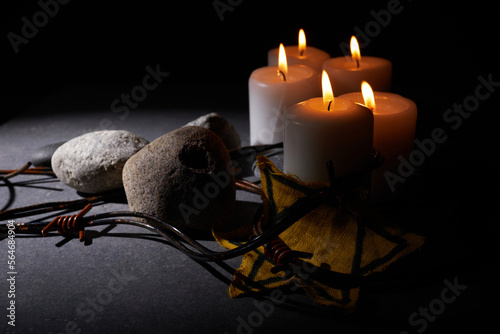 Holocaust memory day. Barbed wire, stones, yellow star and burning candle on black background photo