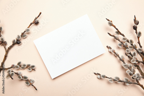 Greeting card mockup with spring floral decor on beige background, top view, flat lay. Blank Easter Holiday card with soft fluffy catkins