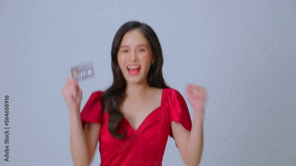 Attractive happy Asian woman smiling charmingly at the camera while standing against a gray-black background in the studio. Happy young female enjoying life holding credit or debit card. Black friday. Attractive happy Asian woman smiling charmingly at the camera while standing against a gray-black background in the studio. Happy young female enjoying life holding credit or debit card. Black friday.