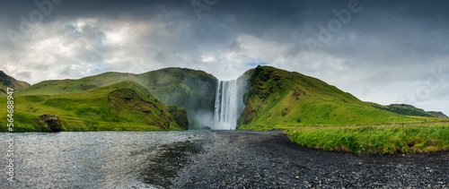 Panorama view of majestic Skogafoss waterfall flowing and moody sky in summer at south of Iceland