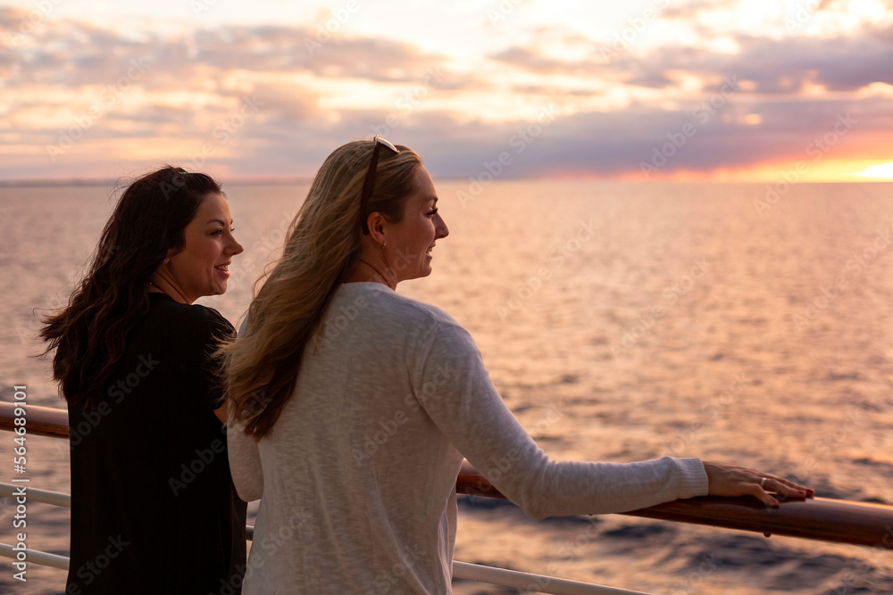 Fototapeta premium Two Attractive middle-aged women enjoying the sunset view from the deck of a cruise ship while on a vacation together in the Caribbean