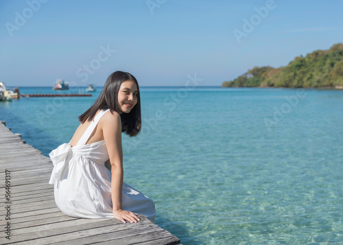 Young asian woman in white dress sitting on wooden pier in tropical sea on sunny day